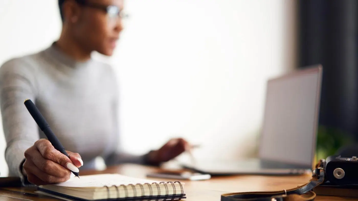Woman in background working on computer and taking notes.